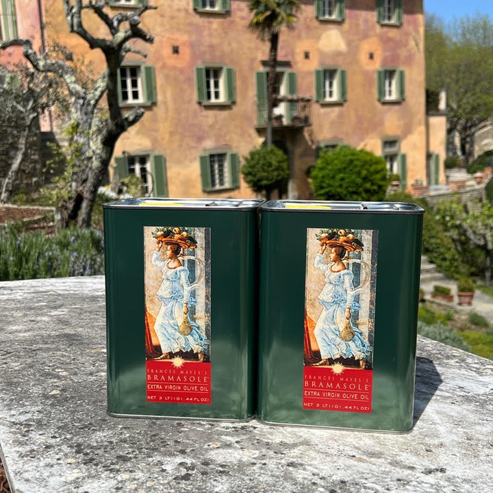 Two green tins with a decorative label on a stone surface, with a building and garden in the background.