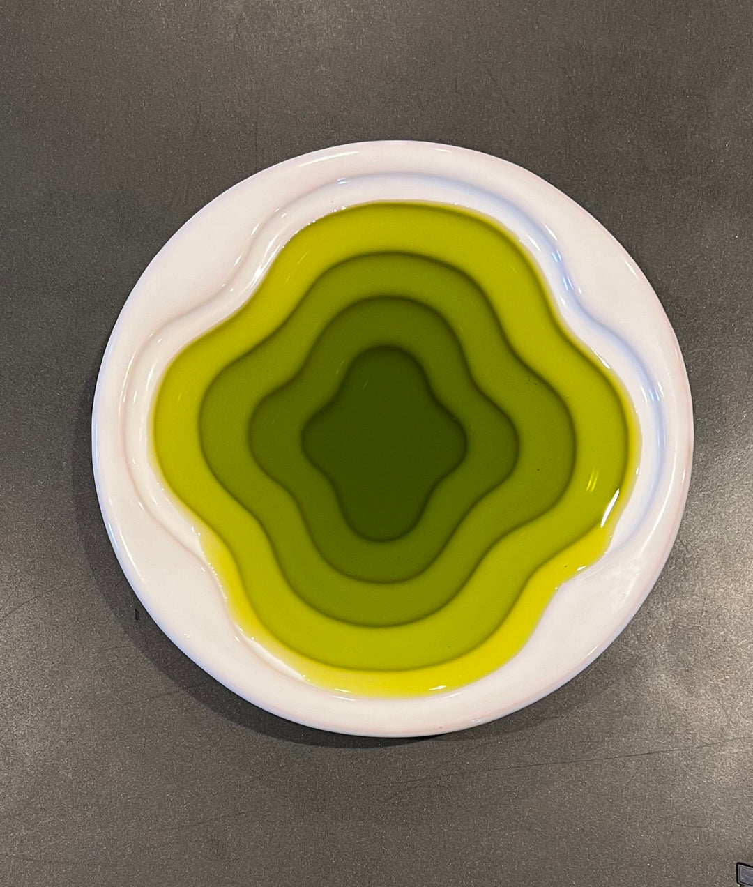 olive oil poured into a white dish with layers to show the deep green of the oil.